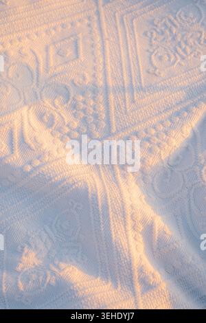 Sunlight highlights patterns on  white textile during early morning hours . Sunlight shines, revealing detailed patterns. soft fabric captures light . Stock Photo