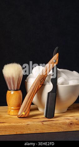 Wooden razor and shaving brush with cream on wooden board in a dark setting Stock Photo
