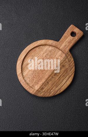 Food, Empty round kitchen wooden cutting board in brown color on a dark textured concrete background Stock Photo