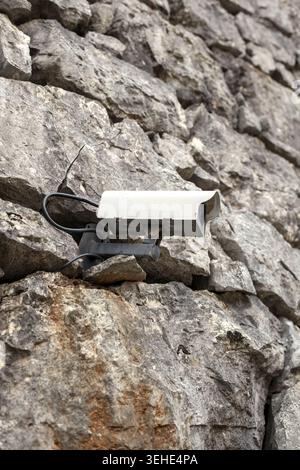 Modern outdoor security camera mounted on a textured ancient stone wall, monitoring safety in a historic area. Stock Photo