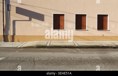 Closed window blinds on plaster facade with pedestrian crossing sign on the left. Sidewalk and street in front. Urban background for copy space Stock Photo