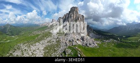 Aerial panoramic view of rugged Dolomite cliffs, green alpine hills and dramatic clouds creating a striking mountain landscape in summer. Stock Photo