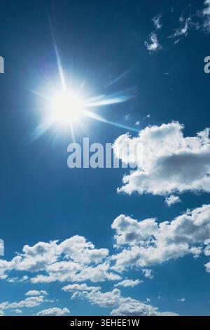 Bright sunburst in a deep blue sky with scattered white clouds, sunny weather and atmospheric copy space Stock Photo