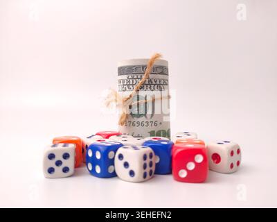 A rolled stack of United States dollar bills secured with twine sits next to a pile of multicolored dice. Stock Photo