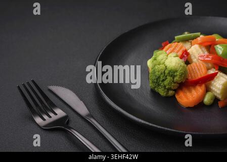 Food, Delicious juicy broccoli vegetables, carrots, asparagus beans, bell peppers steamed in a black plate on a dark concrete background Stock Photo