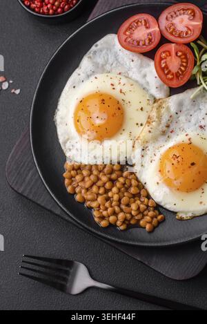 Food, Delicious hearty breakfast consisting of two fried eggs, canned lentils, microgreens with spices and herbs on a dark concrete background Stock Photo
