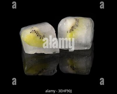 Kiwi slices were frozen inside two ice cubes, on a reflective black background Stock Photo