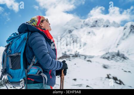 smiling female trekker with large backpack and trekking poles in sharp focus looking up at blurred Eisenerzer Reichenstein mountain in Austria represe Stock Photo
