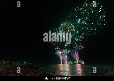 Crowds on the beach watching colorful pyrotechnics lighting up the dark sky and reflecting on the water Stock Photo