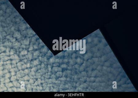 Abstract view of dark building corners forming geometric lines against a blue sky filled with textured cirrocumulus clouds Stock Photo