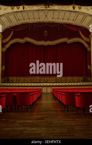 Classic theater with closed red velvet stage curtains and rows of vacant red seats, awaiting a performance Stock Photo