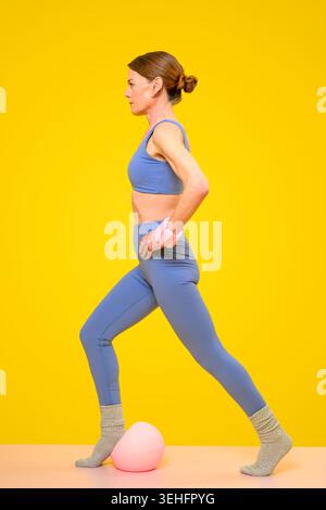 Fit Woman doing a Lunge Exercise With Wrist Weights and Pilates Ball Stock Photo