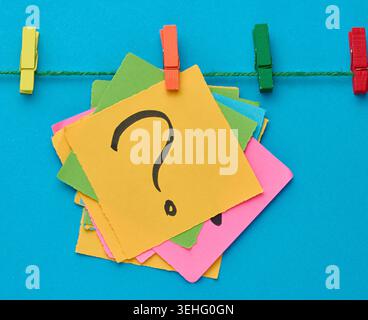 A stack of multi-colored square sticky notes with a question mark on them, attached to a rope with an orange clothespin, a concept of finding a soluti Stock Photo