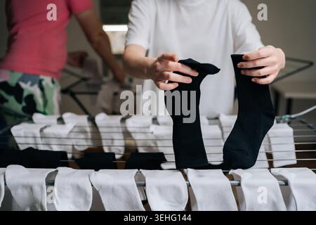Close-up young couple hanging freshly washed laundry on clothes drying rack, placing clean white and black socks on metal bars, performing household Stock Photo