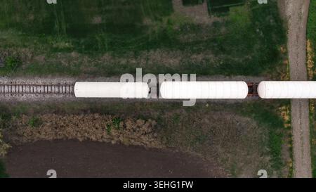 Aerial view of white freight train cars moving along railway tracks through rural farmland, top down Stock Photo