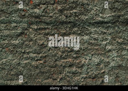 A close-up view of a coarse, uneven concrete wall showing signs of age and wear with hints of reddish-brown undertones as background Stock Photo