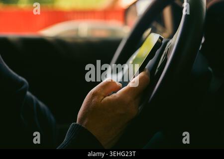 Driver using smartphone while holding steering wheel inside car, distracted driving concept, selective focus Stock Photo