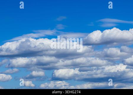 Fluffy white clouds drift across a vast, brilliant blue sky, creating a serene and expansive atmosphere filled with bright, natural daylight. Stock Photo