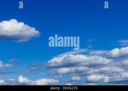 Fluffy white clouds drift across a vast, brilliant blue sky, creating a serene and expansive atmosphere filled with bright, natural daylight. Stock Photo