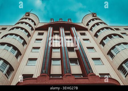Bold red and blue Art Deco lines stretch toward the sky on this striking cream-colored building. The symmetrical towers and retro aesthetic capture th Stock Photo