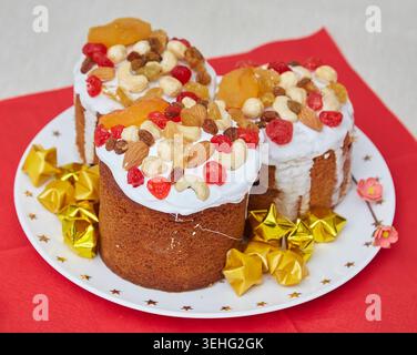 Three small Easter breads, Paska or Kulich, decorated with white frosting, nuts, and dried fruits, on a white plate with gold star decorations. Red na Stock Photo