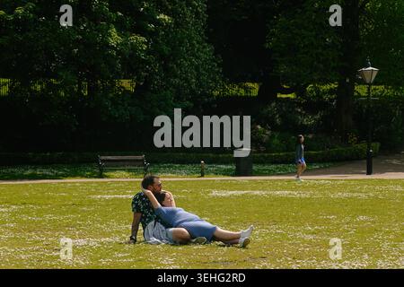 Couple relaxing and lying on a green grass lawn with daisies in Pavilion Gardens, Buxton, Derbyshire, England, UK. Sunny summer leisure day Stock Photo