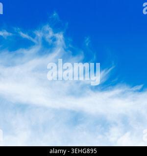 A beautiful clear blue sky with wispy white clouds scattered across  horizon. The scene conveys a sense of tranquility and openness Stock Photo