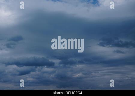 Dark clouds fill the sky with shades of gray and blue, creating a dramatic atmosphere as sunlight breaks through the cloud cover Stock Photo