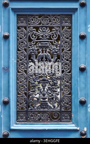Intricate black wrought iron grille featuring floral and animal motifs mounted on a blue wooden door, highlighting decorative artistry and design Stock Photo