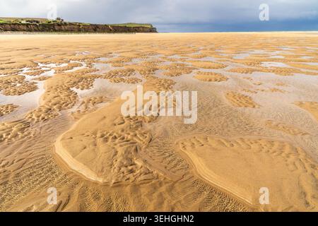 Close-up of spectacular golden sand ripples created by the low tide in Sangatte. Water pools reflect the light, while cliffs and breakwater poles stan Stock Photo