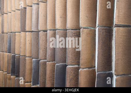 Vertical rows of curved ceramic tiles in mixed brown, grey and white tones forming a geometric pattern texture on a contemporary building wall facade. Stock Photo