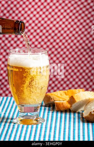 Rustic Oktoberfest inspired scene with fresh beer being poured from a bottle into a glass beside sliced bread on a Bavarian table. Stock Photo