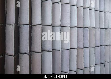 Close up view of a modern architectural wall made of curved ceramic tiles in white, grey and brown colors, showcasing repeating geometric patterns. Stock Photo