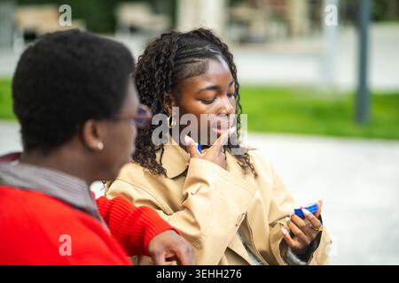 African american woman applying lip balm while spending time outdoors with black male friend. Stock Photo