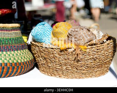 Colorful rolled geometric woven fabrics displayed inside a rustic seagrass basket container at a boutique outdoor market stall. Stock Photo