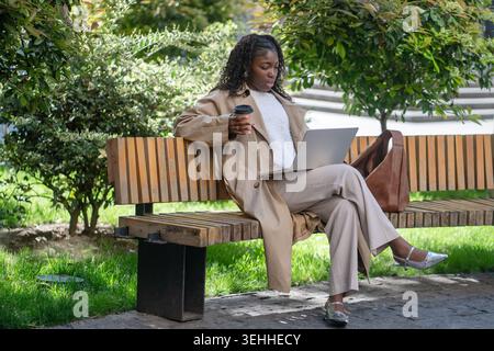 Confident relaxed businesswoman freelancer talking online on laptop by video call sitting in park. Stock Photo