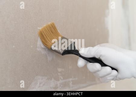 A hand wearing a white glove applies finishing paint to a smooth drywall surface using a high quality brush. Stock Photo