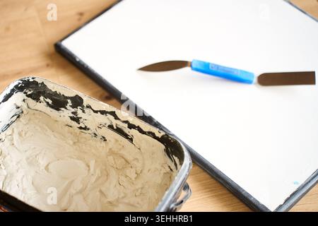 Art tools for textured canvas artwork lie beside white plaster paste and blank canvas on a wooden table. Concept of DIY wall decor and craft preparati Stock Photo