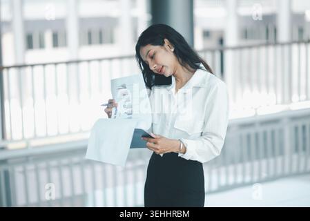 Professional businesswoman balancing a phone on her shoulder while reading financial reports, representing multitasking, mobile communication, documen Stock Photo