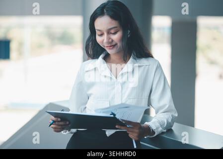 Professional woman reviewing business documents on a clipboard while leaning in a modern office, expressing focused analysis, report checking, organiz Stock Photo