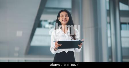 Confident businesswoman smiling while holding a clipboard in a contemporary office, ideal for leadership, recruitment, workplace success, team communi Stock Photo