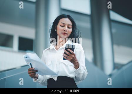 Low angle view of a professional woman speaking on a smartphone and checking documents in a folder, ideal for business communication, client service, Stock Photo