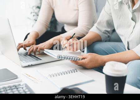 Close-up of two women working on a laptop and taking notes at home, illustrating budget planning, online consultation, remote learning, household fina Stock Photo