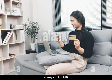 Young Asian woman using smartphone, laptop and credit card for online shopping at home, mobile ecommerce payment, cashless purchase, digital consumer Stock Photo