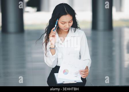 Focused female employee analyzing charts on a clipboard with a pen, showing strategic thinking, financial review, problem solving, decision making, an Stock Photo