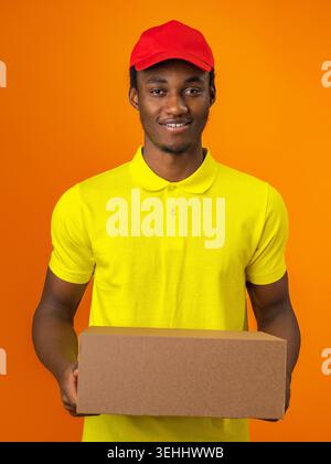 Delivery worker holds a box with a smile against an orange background in bright clothing Stock Photo