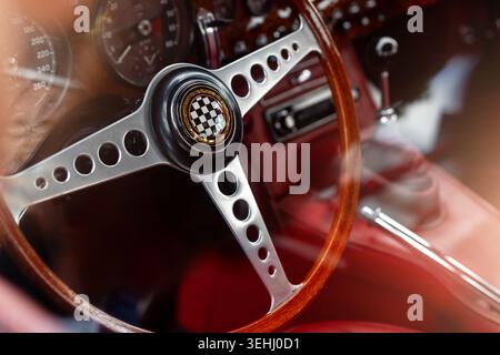 Vintage sports car interior with wooden steering wheel, chrome dashboard and red leather upholstery. Retro cockpit with analog gauges and manual Stock Photo