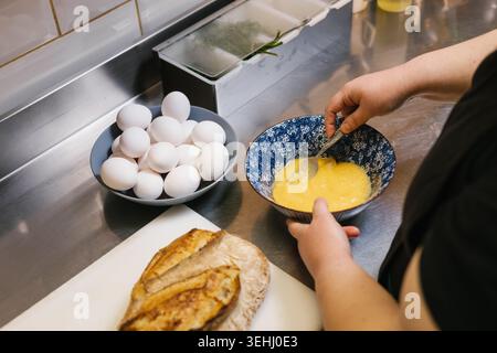 Chef whisking eggs in blue bowl on stainless steel counter Stock Photo