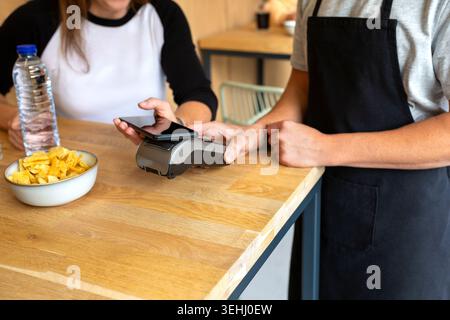 Anonymous customer making contactless payment using smartphone in cafe. Down copy space available. Stock Photo