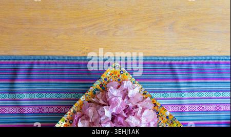 Horizontal composition featuring a vibrant patterned fabric runner on a light wood table next to a dish with pink flowers. Ideal for wellness or bohem Stock Photo